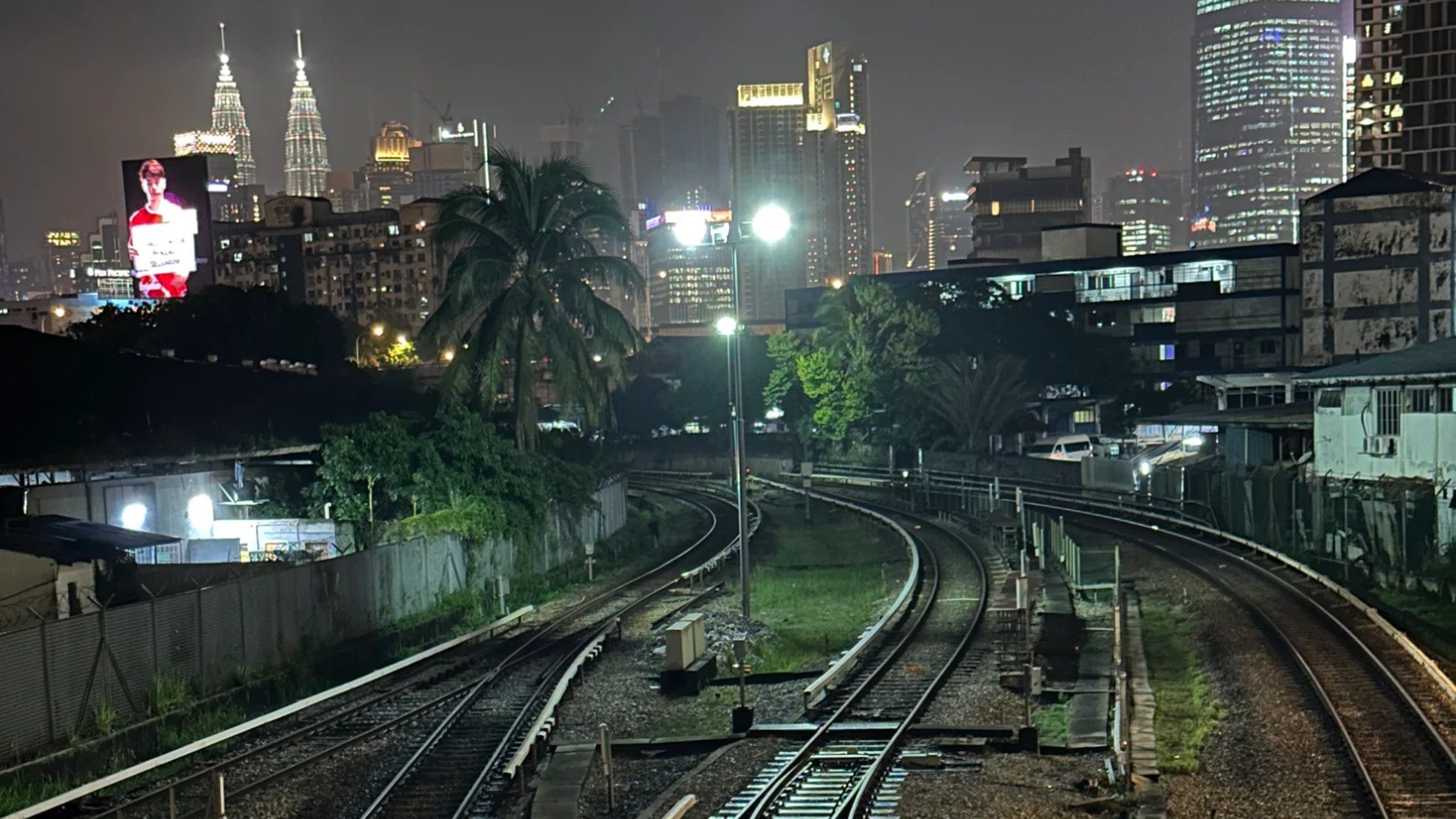 Kuala Lumpur at night: rail tracks stretch into the distance toward the Petronas Towers and Merdeka 118