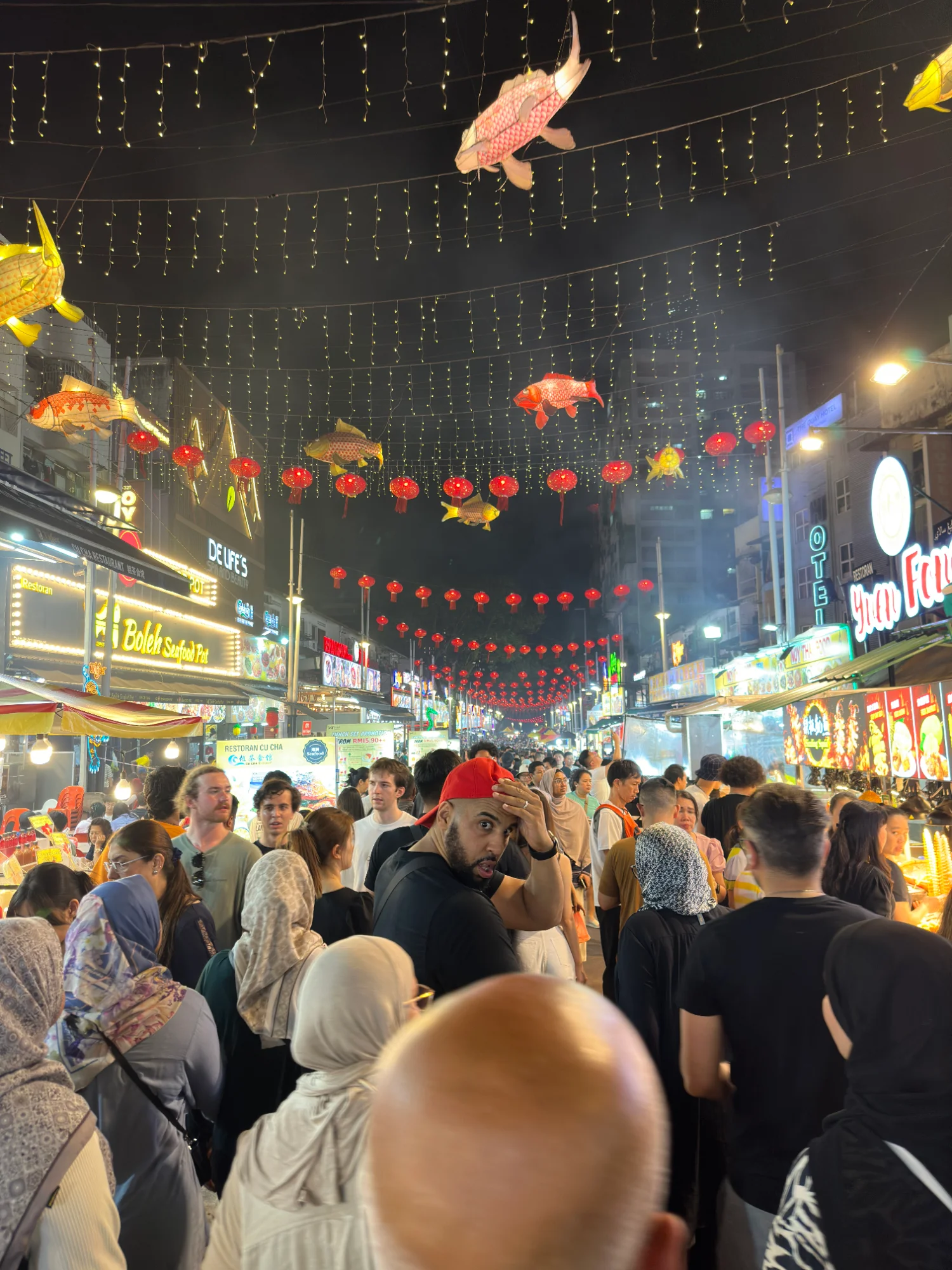 Jalan Alor night market: string lights, red lanterns and koi lanterns overhead, a crowded street and restaurant signs on both sides